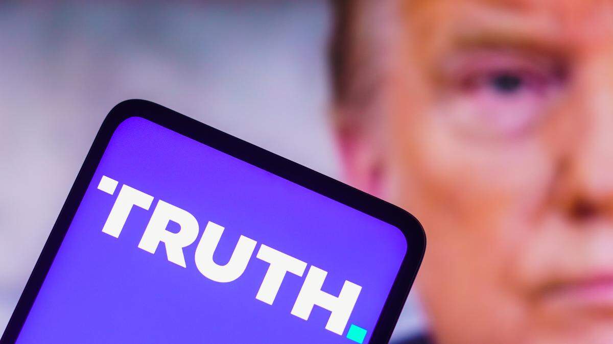 In this photo illustration, the social media platform, Truth Social logo seen displayed on a smartphone with a photo of former US President Donald Trump displayed in the background.