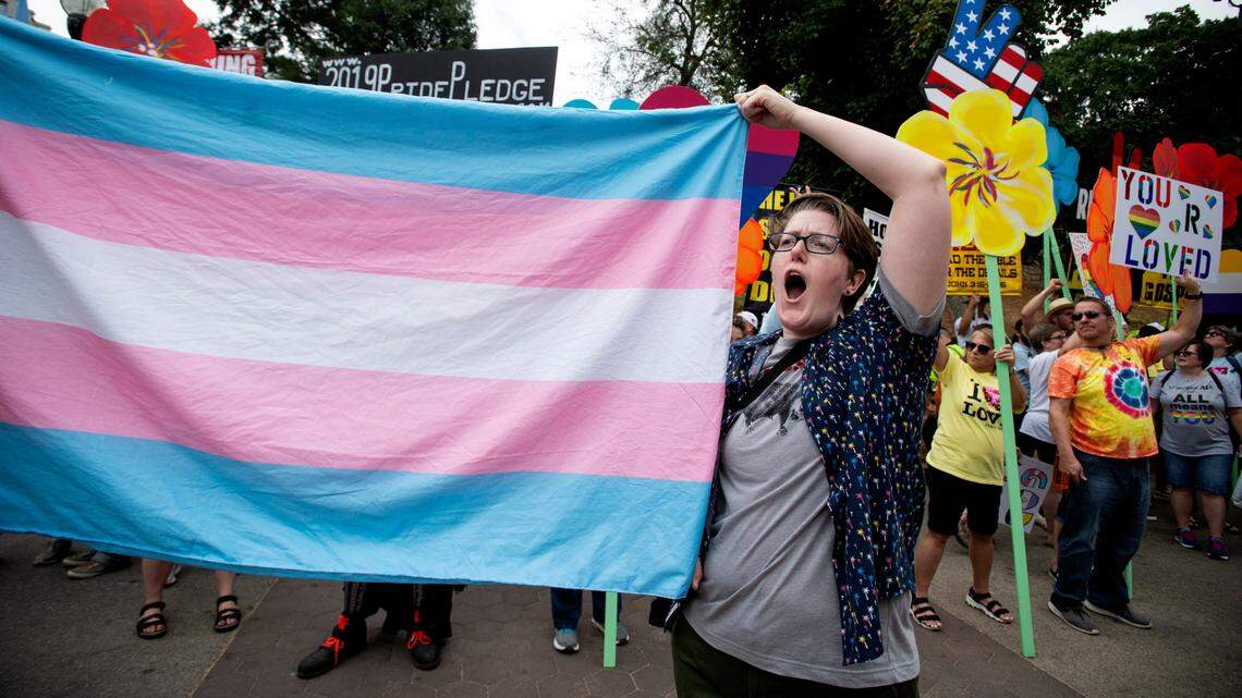 A supporter for the transgender community holds a trans flag in front of counter-protesters to protect attendees from their insults and obscenities at the city’s Gay Pride Festival in Atlanta on Saturday, Oct. 12, 2019. (AP Photo/Robin Rayne)