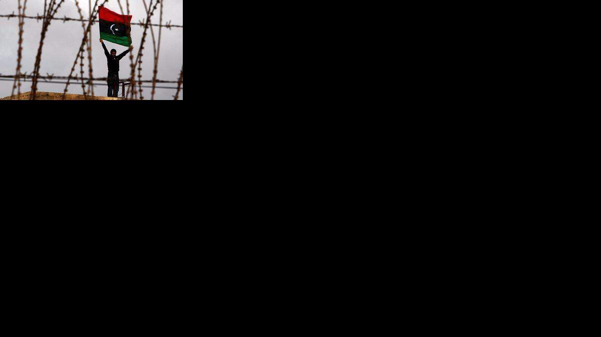 A youth with a flag is framed by the concertina wire surrounding an abandoned Libyan military camp.
