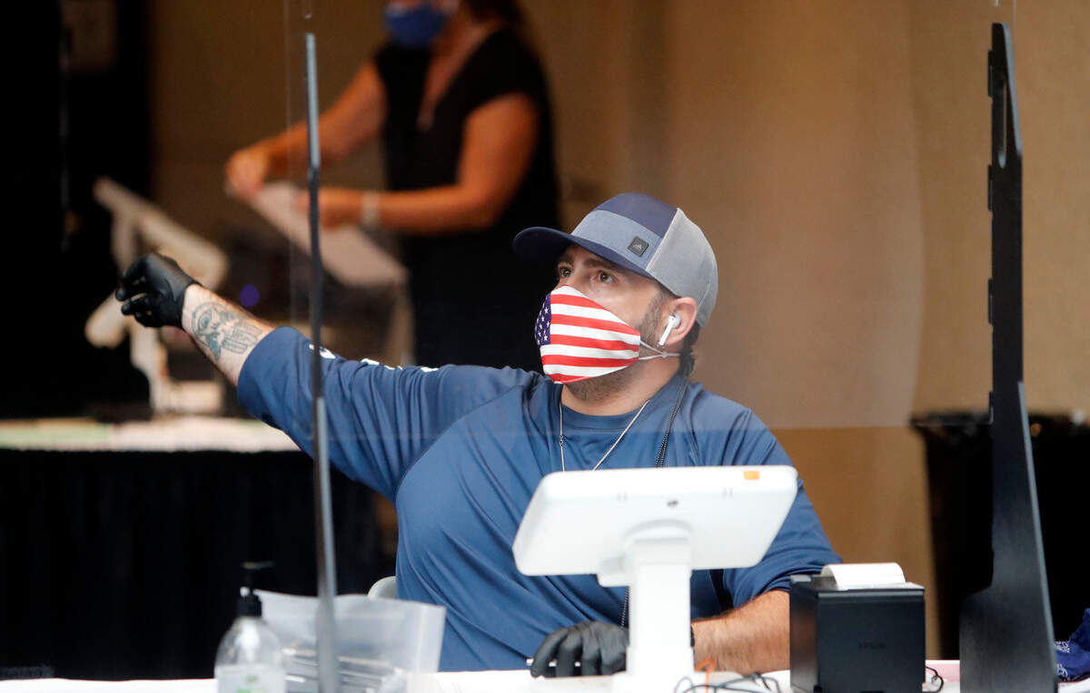 Amid concerns of the spread of COVID-19, Dallas County election worker Mark Bracken wears a mask behind a clear plastic barrier as he directs a voter at a polling station, Tuesday, July 14, 2020, in Richardson, Texas. (AP Photo/LM Otero)