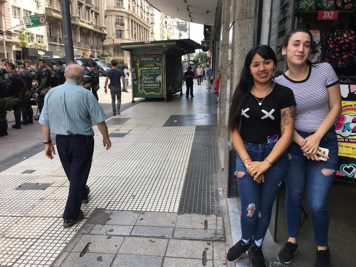 Florencia Ramirez, 27, and Yesica Volpe, 27, stand outside their store in downtown Buenos Aires, Argentina as local police prepare for a large G20 protest on Nov. 30, 2018.
