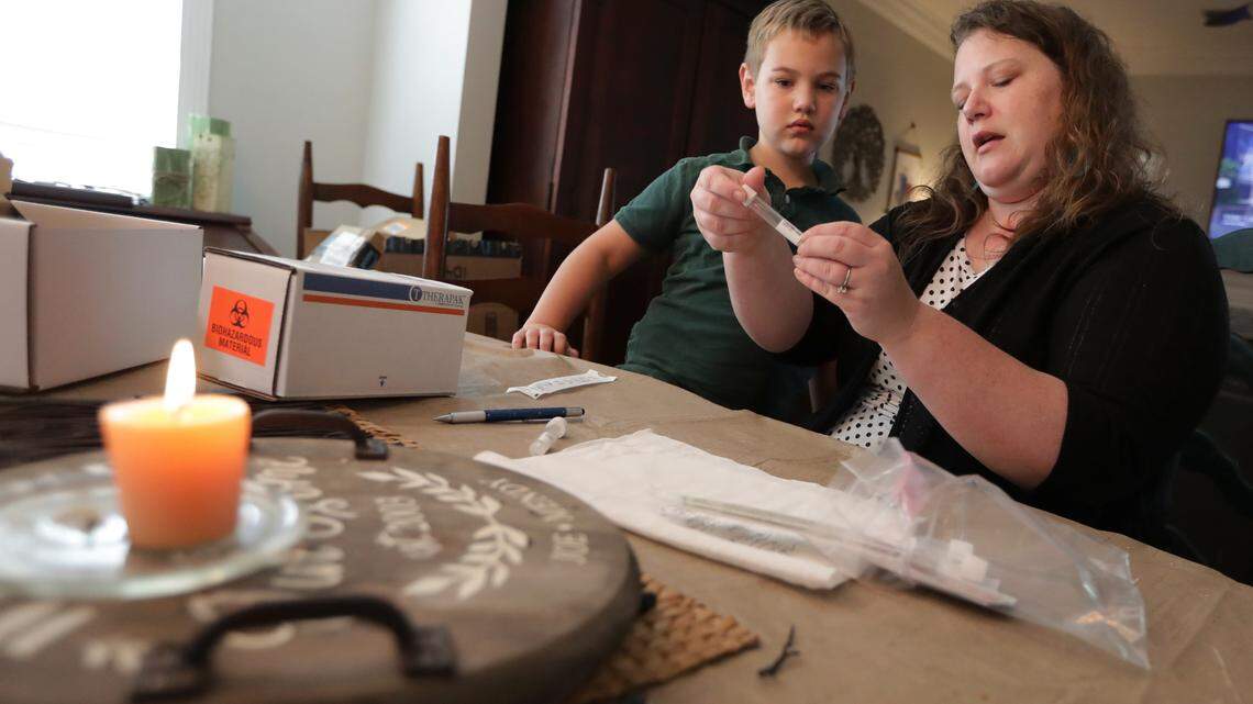 Mendy McNulty prepares test swabs for shipping as her son watches after the family did a twice-weekly coronavirus test in their Tennessee home. The IRS said last week that the costs of at-home COVID-19 testing can be paid for or reimbursed through FSAs, HSA, HRAs and Archer MSAs. (AP Photo/Mark Humphrey)
