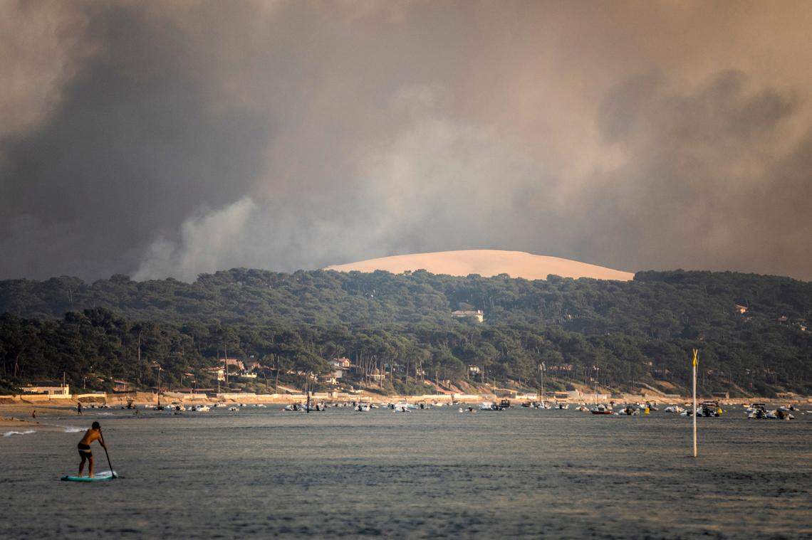 A paddle surfer is seen as smoke laden with ashes coming from a giant wildfire consuming the thousand-year-old forest bordering the Dune du Pilat rises over the beach of Pilat sur Mer, southwestern France, Monday July 18, 2022. France scrambled more water-bombing planes and hundreds more firefighters to combat spreading wildfires that were being fed Monday by hot swirling winds from a searing heat wave broiling much of Europe. (AP Photo/Sophie Garcia)