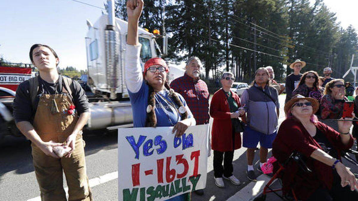 FILE - In this Oct. 17, 2018, file photo, a supporter of Initiative 1631 holds a sign referencing the Nisqually Indian Tribe during a rally supporting I-1631, a November ballot measure in Washington state that would charge a fee on carbon emissions from fossil fuels. Money has poured into the state for the campaign against I-1631, mostly from oil companies.