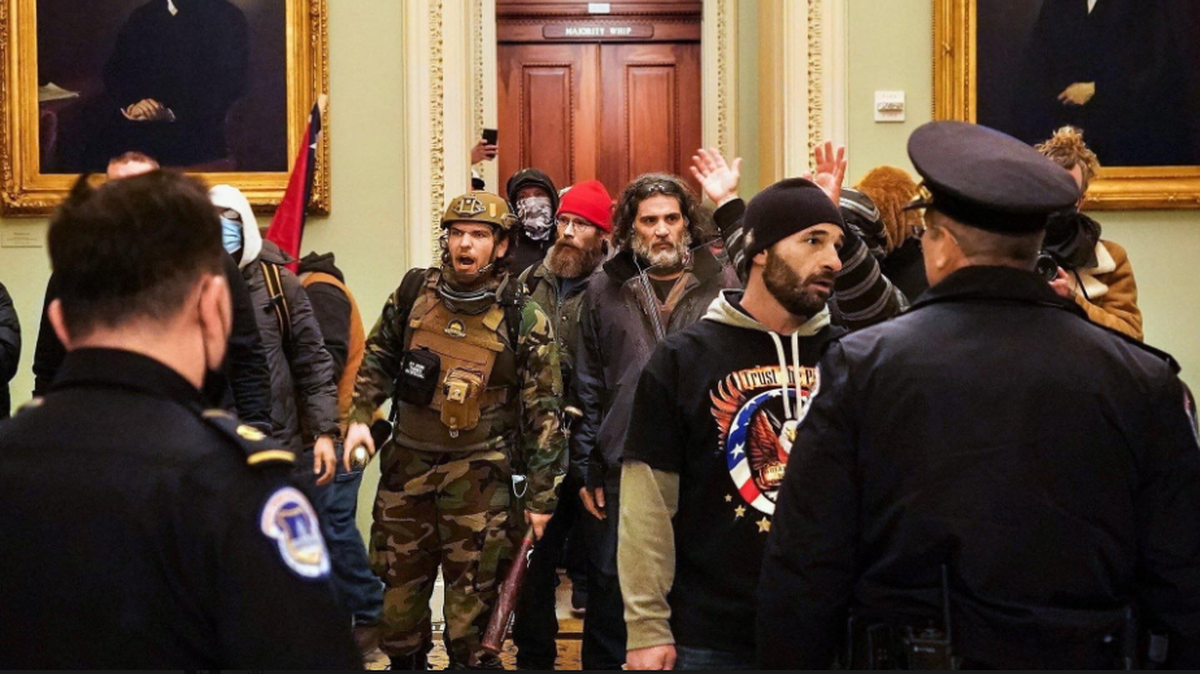 This screenshot of an image widely circulated on social media shows a man carrying a baseball bat and wearing combat gear with an orange tab on his helmet. Several others were seen with orange tab, believed to be a way to signal to others where they were in the angry mob that stormed the Capitol on Jan. 6, 2021.