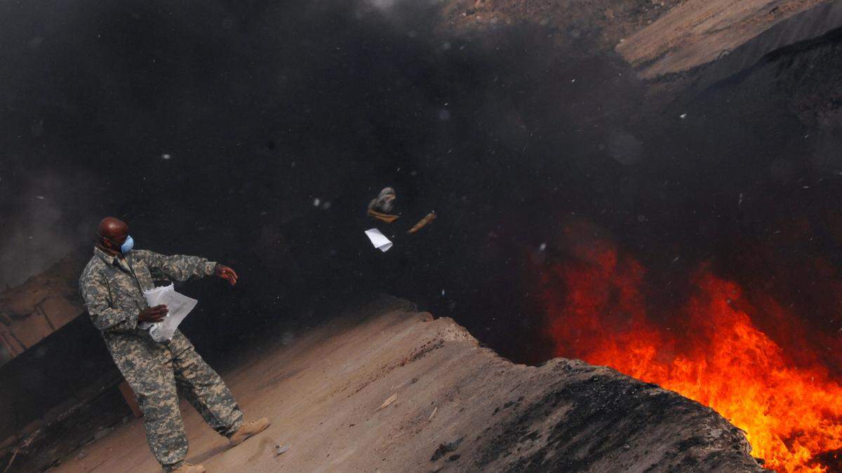 In this March 2008 Department of Defense photo, Master Sgt. Darryl Sterling, 332nd Expeditionary Logistics Readiness Squadron equipment manager, tosses unserviceable uniform items into a burn pit at Balad, Iraq. Uniforms were burned so they would not end up in enemy hands.