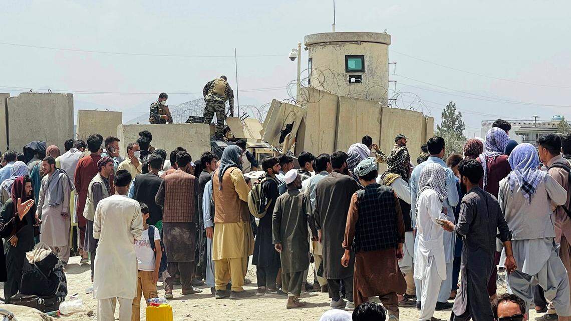 Afghan security guards stand on a wall as hundreds of people gather outside the international airport in Kabul, Afghanistan, on Tuesday. A new poll found support for U.S. withdrawal from Afghanistan has plummeted since April. (AP)
