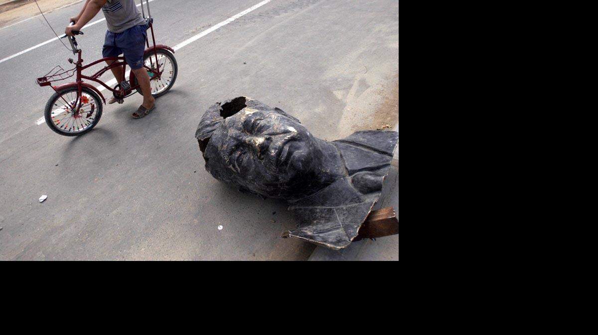 A child rides by the head of the Saddam Hussein monument taken down from Paradise Square in Baghdad in April 2003.