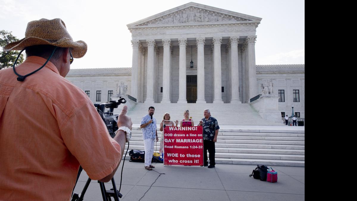 
A television crew records protestors outside of the Supreme Court in Washington, Thursday June 25, 2015. The court is expected to hand down decisions today. Two major opinions, health care and gay marriage, are among the remaining to be released before the term ends at the end of June. 
