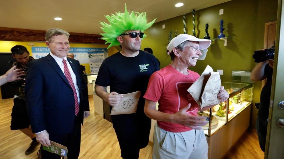 Seattle City Attorney Pete Holmes, left, Jeremy Cooper and Deb Greene walk out after being among the first customers to legally purchase recreational pot in Seattle at Cannabis City, on July 8, 2014. When Holmes took the pot to his office, he inadvertently violated the city’s drug-free workplace policy. Now he says it’s time for Americans to have an “overdue conversation” on marijuana in the workplace.