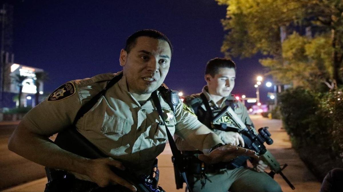 On the Las Vegas Strip, police officers advise people to take cover near the scene of a mass shooting outside the Mandalay Bay resort and casino on Sunday, Oct. 1.