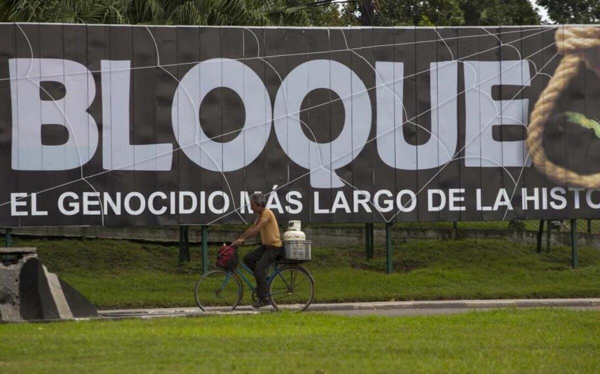 A man carries a gas cylinder on the back of his bicycle as he passes a billboard that reads in Spanish "Blockade: The longest genocide in history" in Havana on Jan. 26, 2016.