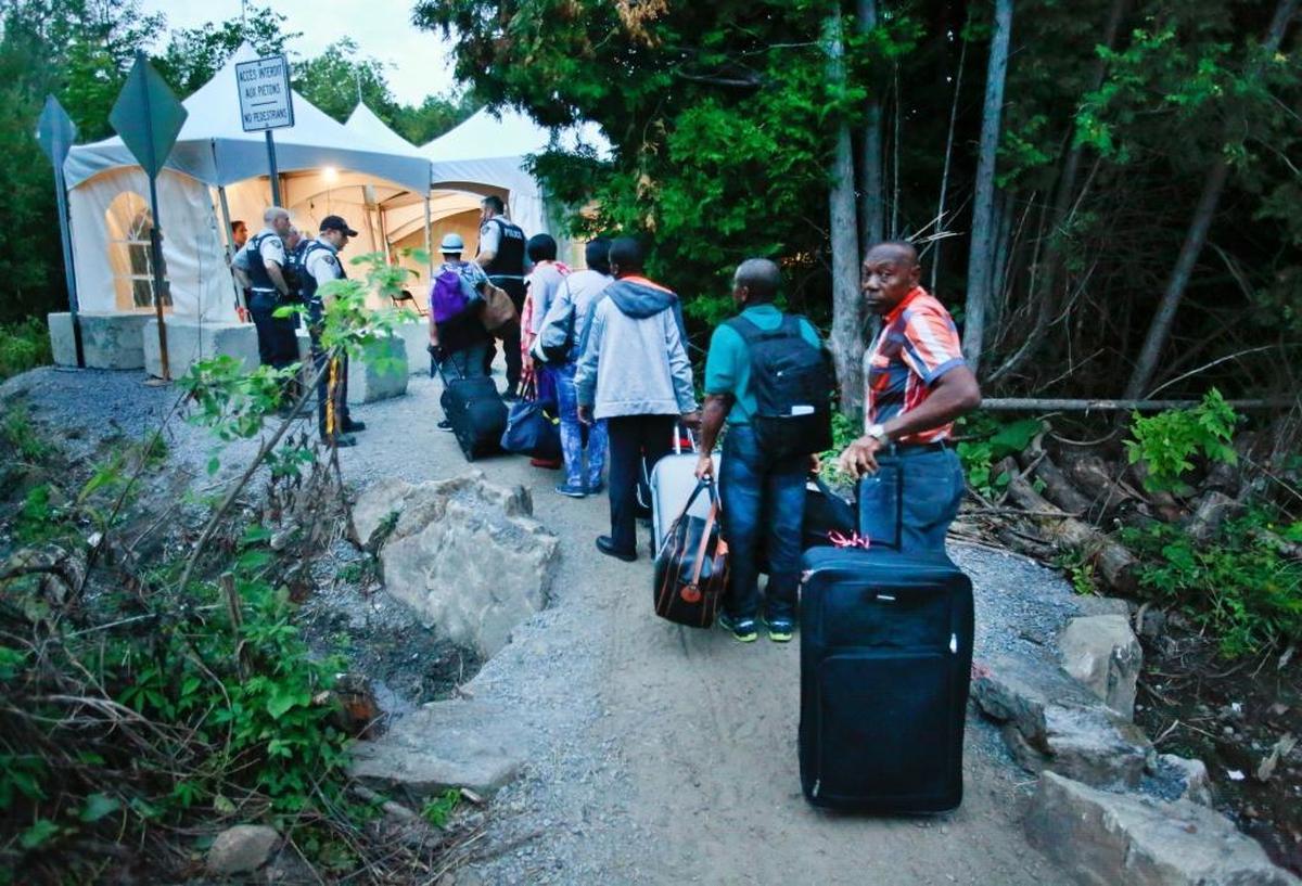 In this file art, Haitian migrants living in the US prepare to cross the US and Canadian border along Roxham Road on Friday, August 11, 2017. Thousands of Haitians have crossed over in to Canada from an irregular crossing near the Champlain-Saint-Bernard-de-Lacolle border in hopes of finding residency in Canada.