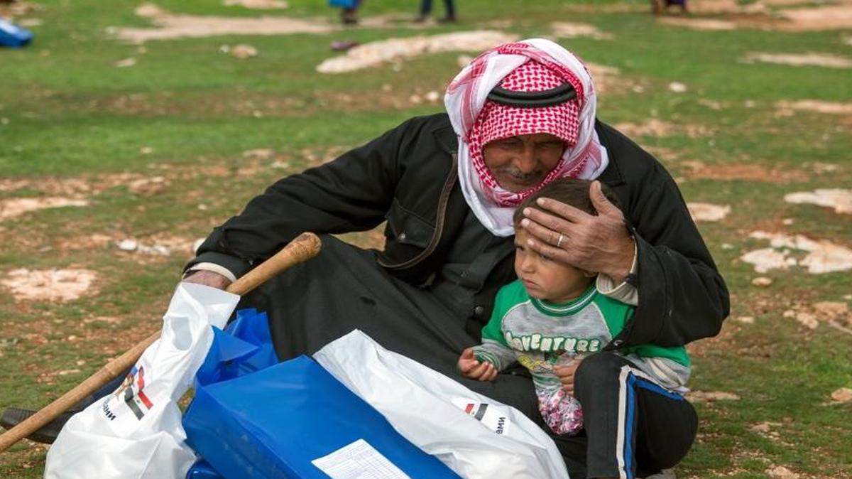 A man and a child sit with an aid package they received from the Russian military near Maarzaf, Syria, on Wednesday. Russian defense ministry spokesman Maj. Gen. Igor Konashenkov said Russia has delivered around 580 tons of food aid to government-held areas since it began airstrikes in support of Syria's government in September 2015. U.S. officials in Washington said a lull in fighting has allowed the delivery of aid to 100,000 people in besieged areas.