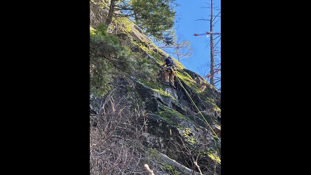 A rescuer is seen climbing up steep terrain to reach the injured climber at Beacon Rock State Park.