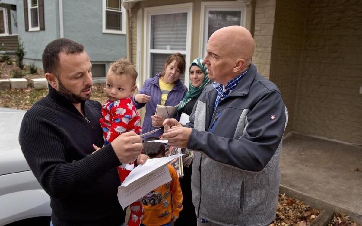A Syrian refugee family that recently arrived in Independence includes the father, Ibraheem Alkhwaja (left), shown holding his 1-year-old son Mohamad. Alkhwaja’s wife is Enas Hajah (second from right); the family is being helped by neighbors Jeff Rogers (right) and Cindi Rogers (third from left). The family’s saga began when they fled violence in Syria three years ago. Here the neighbors help the refugees understand their mail.