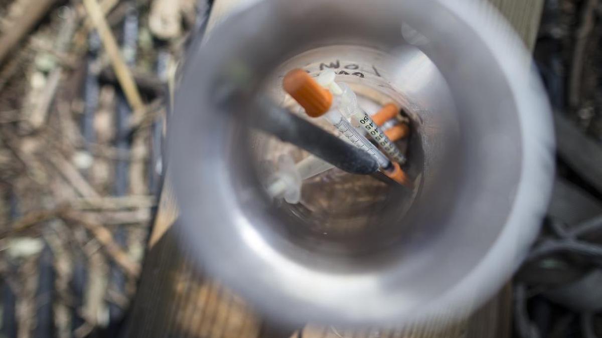 In this Thursday, Sept. 17, 2015, photo, used heroin syringes are stored in a water bottle as Steve Monnin cleans a wooded area in Combs Park, in Hamilton, Ohio.