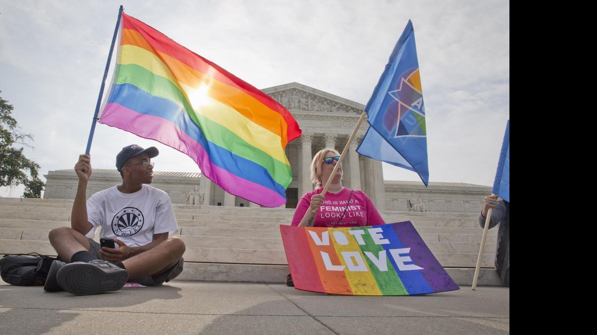 
Carlos McKnight, 17, of Washington, left, and Katherine Nicole Struck, 25, of Frederick, Md., hold flags in support of gay marriage outside of the Supreme Court in Washington, Friday June 26, 2015. A major opinion on gay marriage is among the remaining to be released before the term ends at the end of June. 
