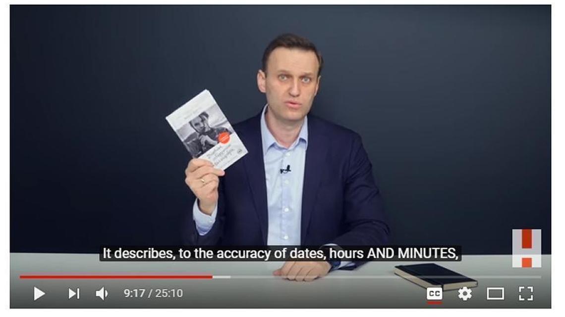 A screenshot of video by Russian opposition leader Alexei Novalny. He is shown holding a book purportedly written by a female escort about a yacht trip by a Russian oligarch and the country’s deputy prime minister, allegedly traveling incognito in the company of prostitutes.