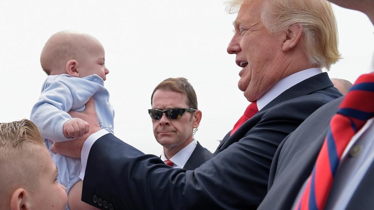 President Donald Trump picks up a baby as he greets people after arriving on Air Force One at General Mitchell International Airport in Milwaukee, Tuesday, April 18, 2017.