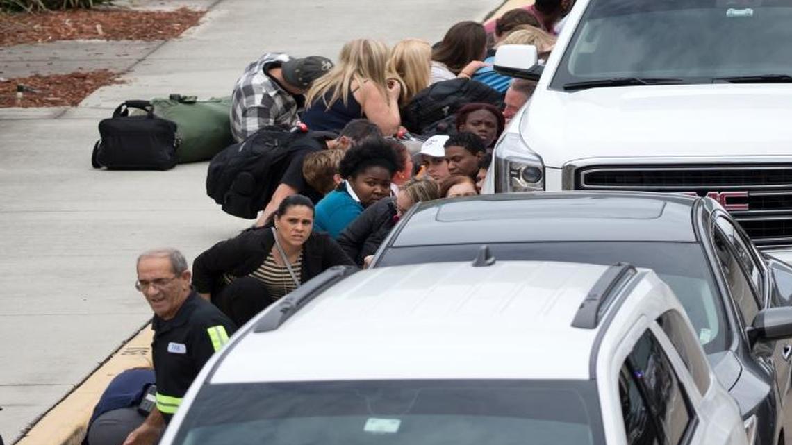 People take cover outside Fort Lauderdale–Hollywood International Airport, Friday, Jan. 6, 2017, after a shooter opened fire inside a terminal of the Florida airport, killing several people and wounding others before being taken into custody.