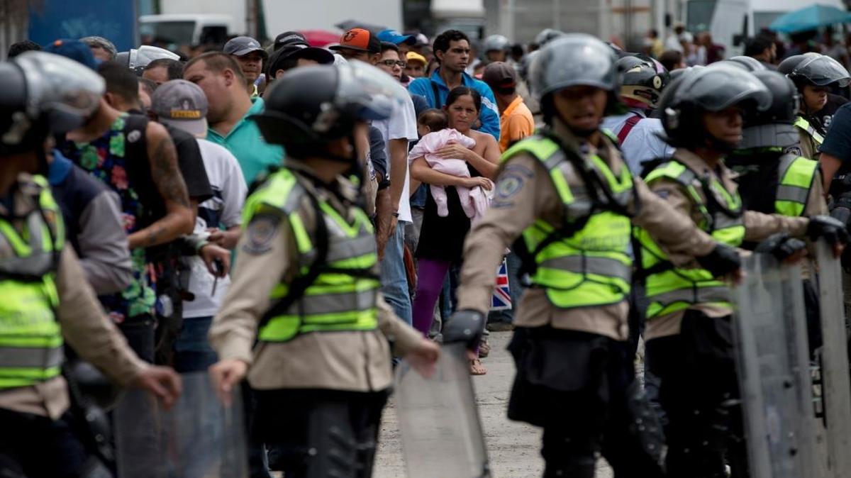 A woman holding a baby looks at police in riot gear standing guard as she and others wait outside a supermarket to buy food in Caracas, Venezuela in this June 1, 2016 file photo. A new Gallup polls found that citizens in Venezuela feel less safe in their country than citizens in Syria.