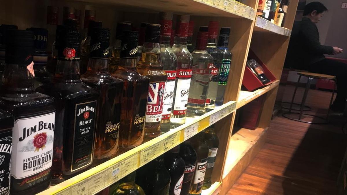 A worker sits near a shelve displaying bottles of American whiskey for sale at a supermarket in Beijing Wednesday.