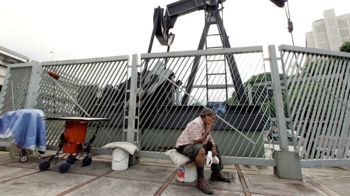 Homeless woman Carmen Elena Sanchez smokes a cigarette under a sculpture of an oil drill in Caracas, Venezuela on May 31, 2006