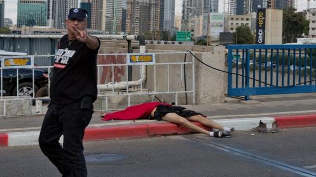 
The body of a Palestinian man accused of stabbing five Israelis with a screwdriver in Tel Aviv, Israel, Thursday lay on the street after he was shot a killed. A passing police officer is gesturing at the photographer.
