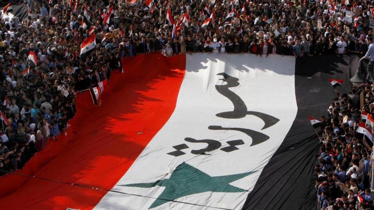 Pro-Syrian regime protesters, carry a giant Syrian flag during a demonstration against the Arab League decision to suspend Syria, in Damascus, Syria, on Sunday Nov. 13, 2011. Tens of thousands of pro-regime demonstrators gathered in a Damascus square Sunday to protest the Arab League's vote to suspend Syria over its bloody crackdown on the country's eight-month-old uprising.