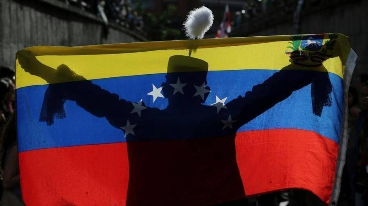 A demonstrator dressed as Venezuelan independence hero Simón Bolivar is silhouetted against a national flag during a tribute to the dead on July 24 in Venezuela.
