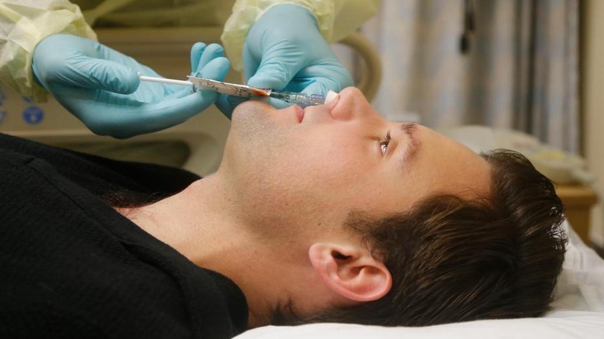 In this Jan. 14, 2014, photo, Daniel Bennett, 26, of College Park, Md., has live flu virus sprayed into his nose as part of a study at the National Institutes of Health in Bethesda, Md.