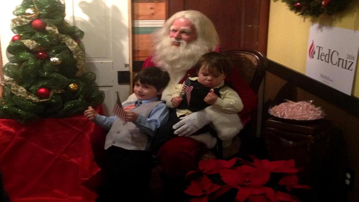 Four-year-old Jonathan Schupe, left, and his 18-month-old brother, Harrison Schupe, sit on the lap of Santa Claus, as portrayed by Robin Hood, before a Ted Cruz rally in Mechanicsville, Va, on Friday, Dec. 18, 2015.