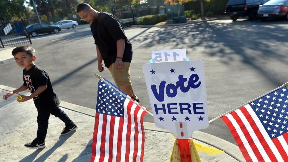 Antwone Atterberry Burrell, 6, left, and his father, Delbon Atterberry Burrell, both of Fresno, Calif.., walk past voting signs for the presidential election on Tuesday, Nov. 8, 2016, at the Boy Scouts of America polling place in northwest Fresno.