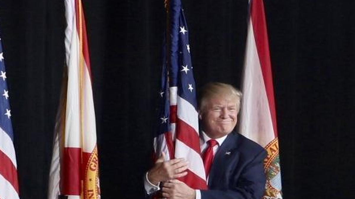 Republican presidential candidate Donald Trump hugs an American flag as he arrives to speak to a campaign rally in Tampa, Fla., Monday, Oct. 24, 2016.