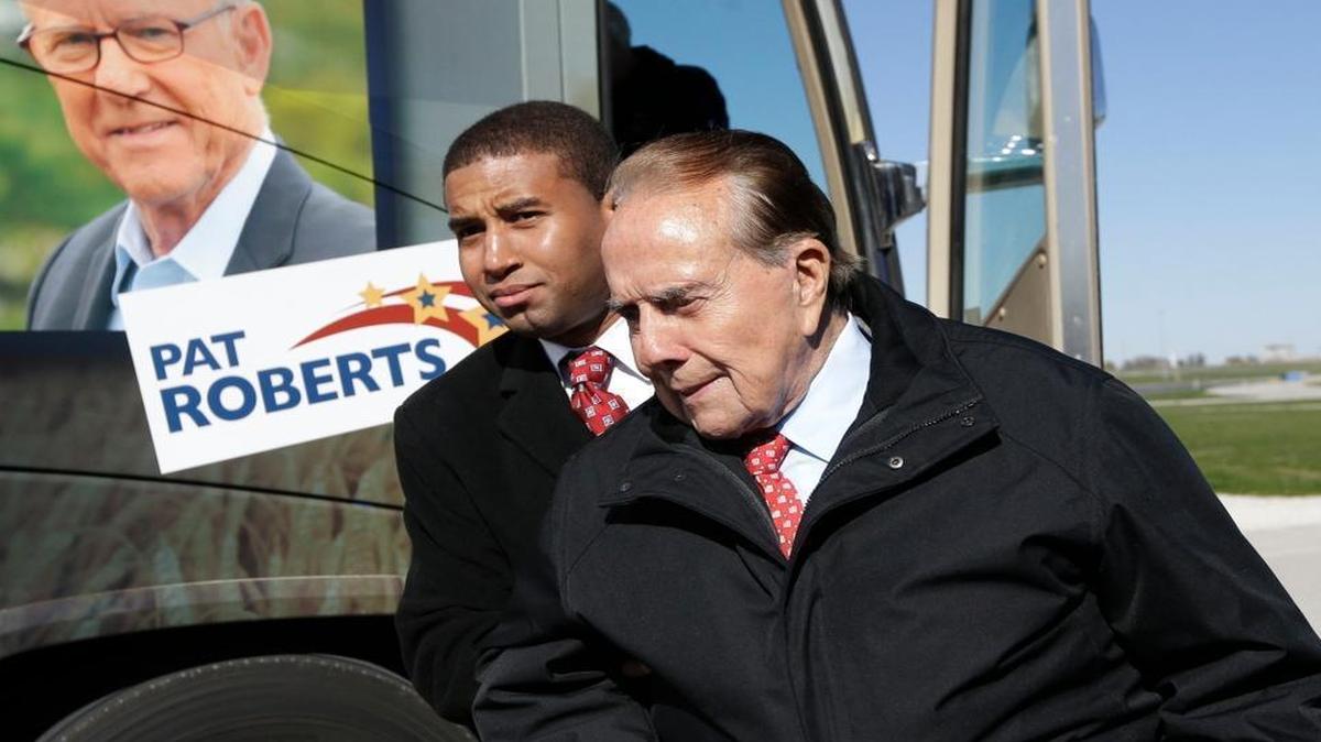 Former Sen. Bob Dole, R-Kan., is helped to his position during a campaign stop in support of Sen. Pat Roberts and Gov. Sam Brownback in Kansas City, Kan., on Friday, Oct. 31, 2014.