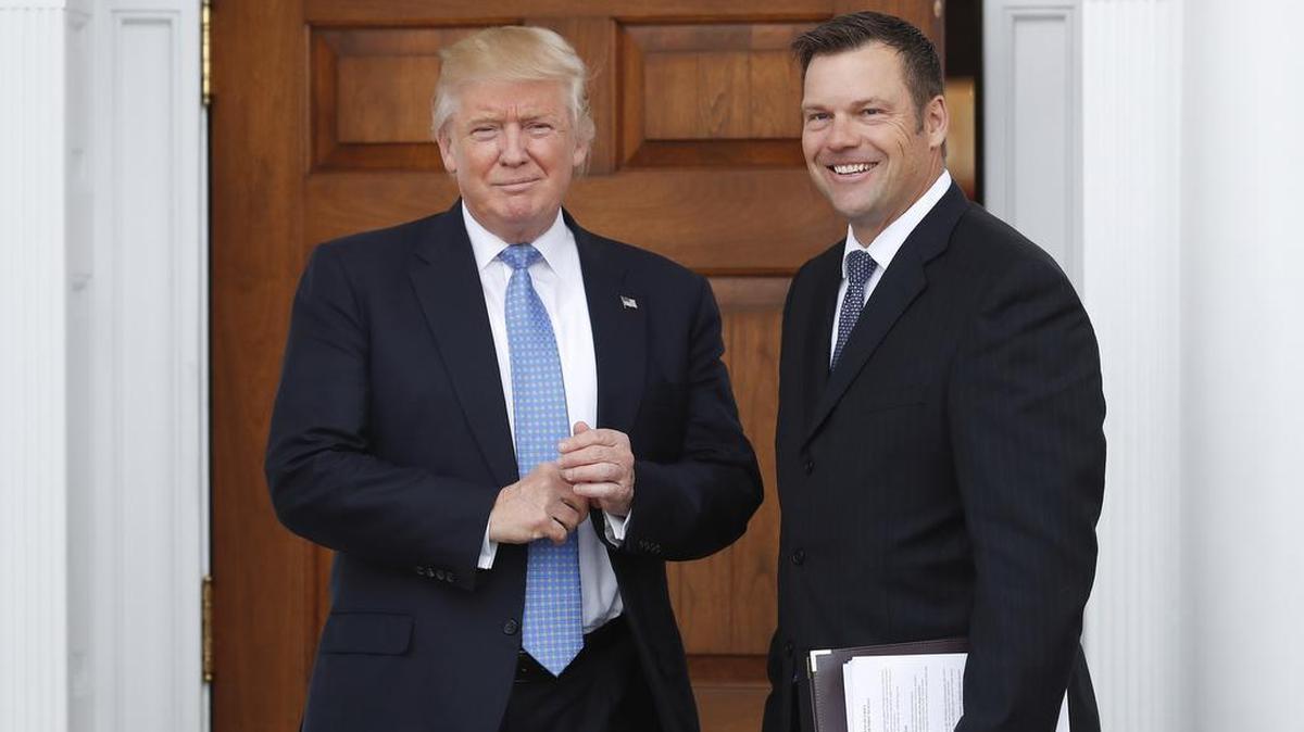 Kansas Secretary of State Kris Kobach, right, holds a stack of papers as he meets with then President-elect Donald Trump.