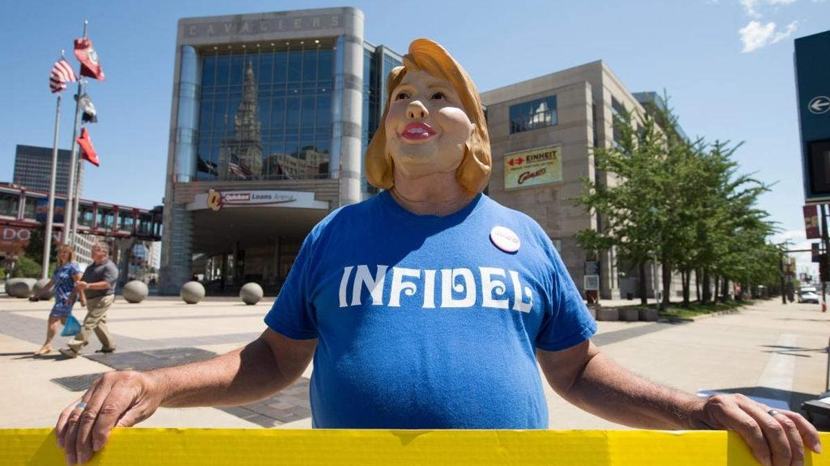
Bob Kunst of Miami Beach, Fla. wears a Hillary Clinton mask and holds an anti-Hillary poster outside the Quicken Loans Arena in Cleveland, site of Thursday’s Republican debate. 
