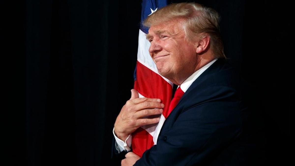 Republican presidential candidate Donald Trump hugs an American flag as he arrives to speak to a campaign rally, Monday, Oct. 24, 2016, in Tampa, Fla.