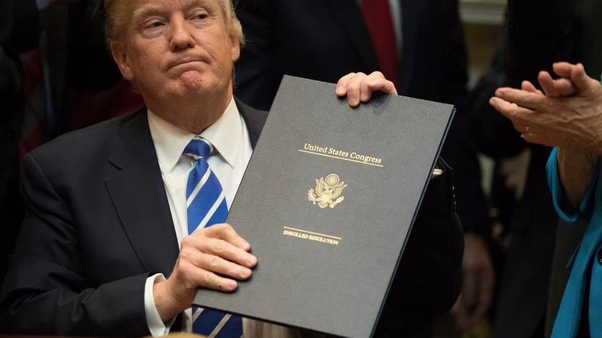 President Donald Trump holds up one of various bills he signed, Monday, March 27, 2017, in the Roosevelt Room of the White House in Washington.