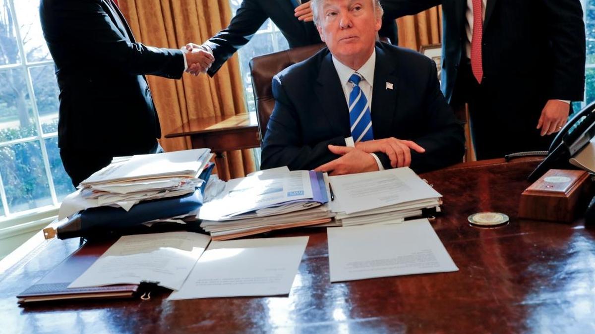 President Donald Trump sits at his desk after a meeting with Intel CEO Brian Krzanich, left, and members of his staff in the Oval Office.