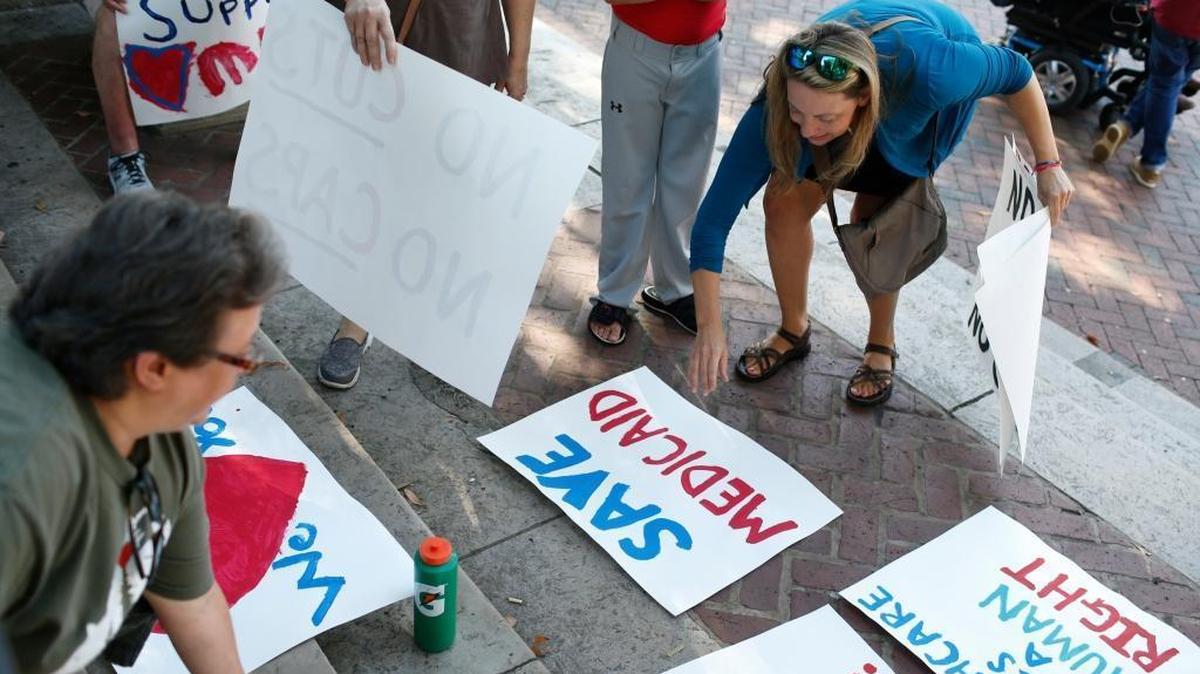 Rally organizer Jill Gambill, right, lays out protest signs just before a rally organized by Gambill and other mothers of special needs children and Athens for Everyone at the University of Georgia Arch for Callie Moore a 22-year-old with cerebral palsy and those like her that would be negatively affected by the Senate health care bill and cuts to Medicaid in Athens, Ga., on Wednesday, July 12, 2017. Moore is unable to walk or speak and requires 24-hour care on July 4, she snapped her femur while being lifted from her bed and Is currently hospitalized. 75 protesters filled the steps and sidewalk at the UGA Arch during the rally. (Joshua L. Jones/Athens Banner-Herald via AP)