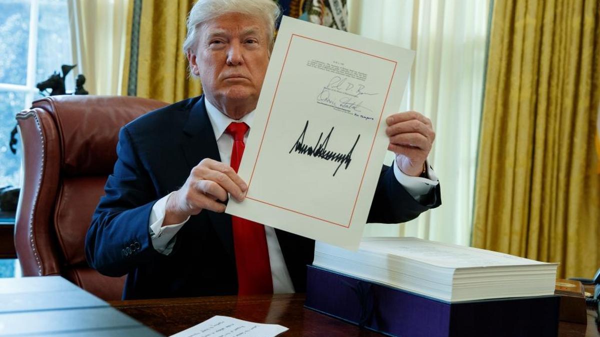 President Donald Trump shows off the tax bill after signing it in the Oval Office of the White House, Friday, Dec. 22, 2017, in Washington.
