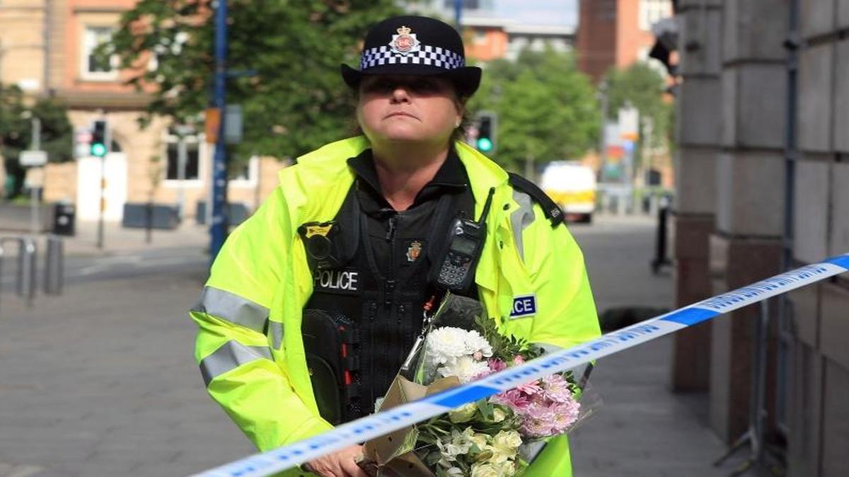 A police officer carries a floral tribute close to the Manchester Arena, the morning after a suicide bomber killed more than a dozen people as an explosion tore through fans leaving a pop concert in Manchester, England, Tuesday, May 23, 2017.