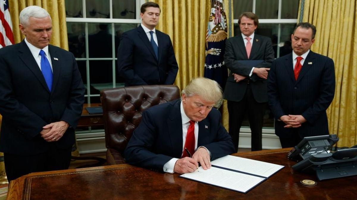 President Donald Trump, flanked by Vice President Mike Pence and Chief of Staff Reince Priebus, signs his first executive order on health care, Friday, Jan, 20, 2017, in the Oval Office of the White House in Washington.
