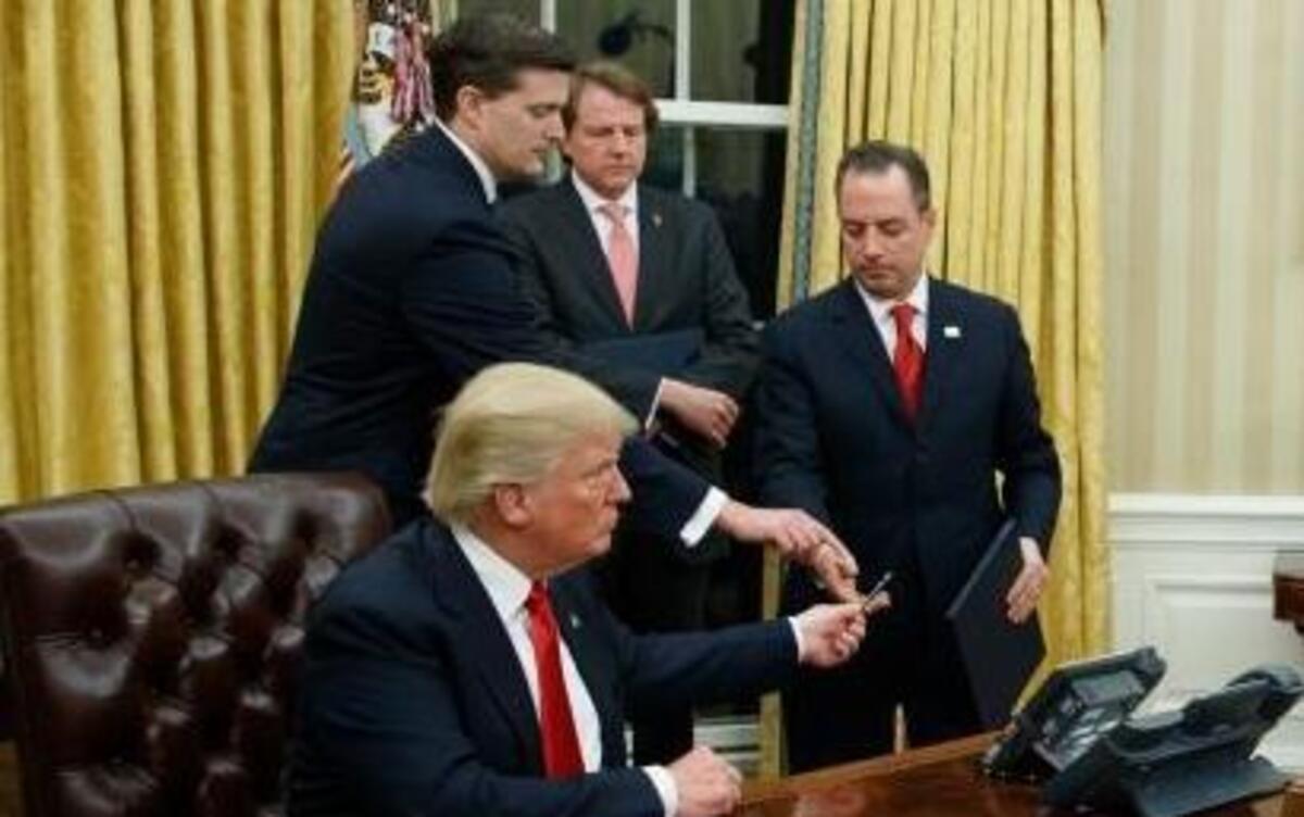In this Jan. 20, 2017, photo, President Donald Trump hands over his pen after signing his first executive order in the Oval Office of the White House in Washington. Itâ€™s the first full work week for the Trump administration, and the talk is all about emoluments, executive orders, a border tax, TPP and much more.