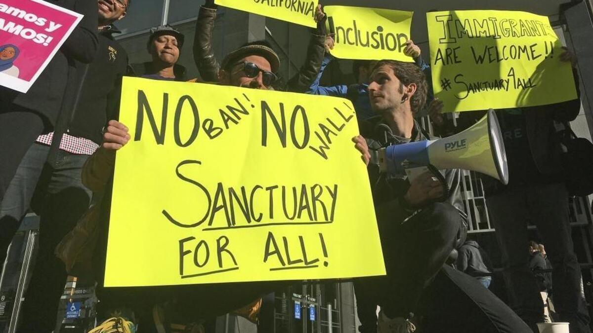 FILE - In this April 14, 2017, file photo, protesters hold up signs outside a courthouse where a federal judge will hear arguments in the first lawsuit challenging President Donald Trump's executive order to withhold funding from communities that limit cooperation with immigration authorities in San Francisco. A federal judge in San Francisco will not immediately require the Trump administration to award California a law enforcement grant that the administration has held over concerns the state does not comply with immigration law. U.S. District Judge William Orrick on Monday, March 5, 2018, rejected the state's request for a preliminary injunction to turn over the money.