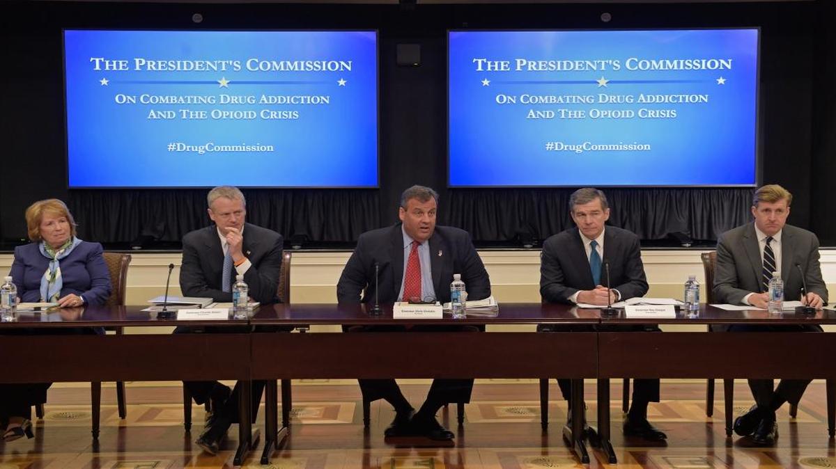New Jersey Gov. Chris Christie, center, chairman of the President's Commission on Combating Drug Addiction and the Opioid Crisis, peaks at the beginning of the first meeting of the commission on combating drug addiction and the opioid crisis, Friday, June 16, 2017, in the Eisenhower Executive Office Building at the White House complex in Washington. From left are , Dr. Bertha K. Madras, a Harvard Medical School professor who specializes in addiction biology, Massachusetts Gov. Charlie Baker, Christie, North Carolina Gov. Roy Cooper, and former Rhode Island Rep. Patrick Kennedy.