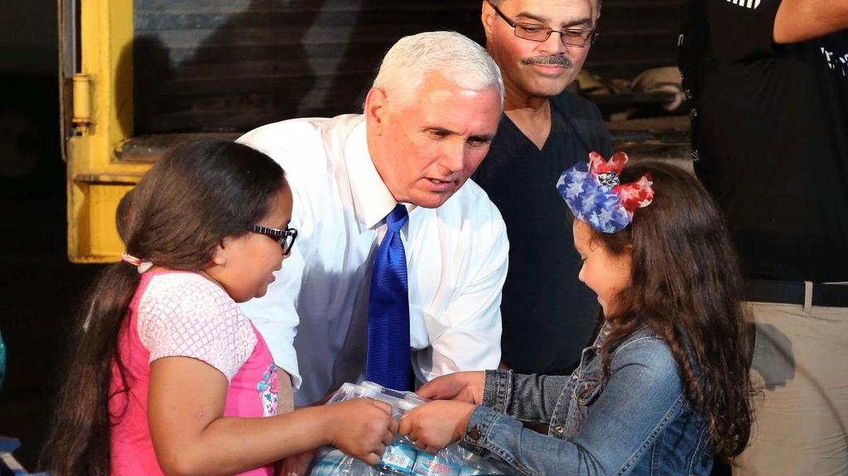 Emma Perez, 9, left, and Summer Muñoz, 7, hand Vice President Mike Pence a case of bottled water Thursday as he helps load a container bound for Puerto Rico, while visiting volunteers working on the relief effort for victims of Hurricane Maria at the Iglesia de Dios church in Kissimmee.