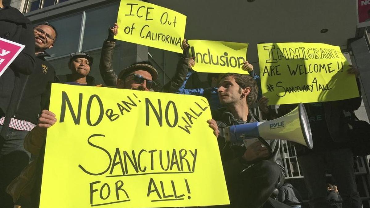 Protesters hold up signs outside a courthouse where a federal judge will hear arguments in the first lawsuit challenging President Donald Trump's executive order to withhold funding from communities that limit cooperation with immigration authorities, April 14, 2017, in San Francisco.